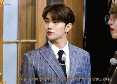 A Man In A Suit And Tie Stands Next To Another Man In Glasses And Red Lipstick GIF