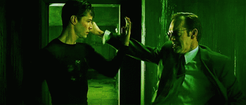 A Man In A Suit And Tie Stands Next To Another Man GIF