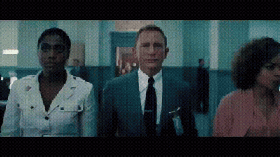 A Man In A Suit And Tie Stands Next To Two Women In A Hallway GIF