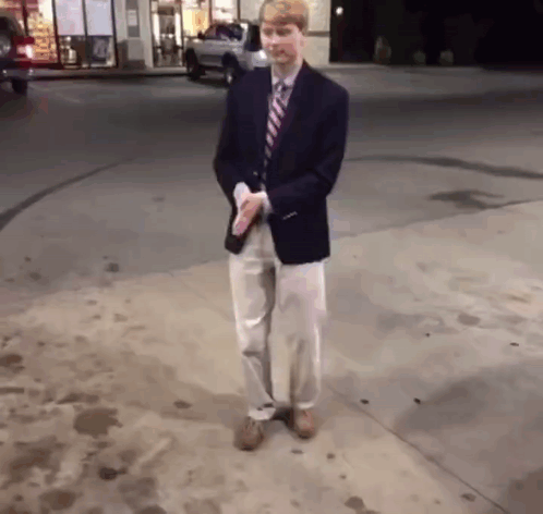 A Man In A Suit And Tie Stands On A Sidewalk GIF