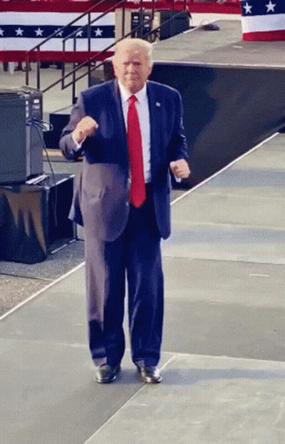 A Man In A Suit And Tie Stands On A Stage GIF