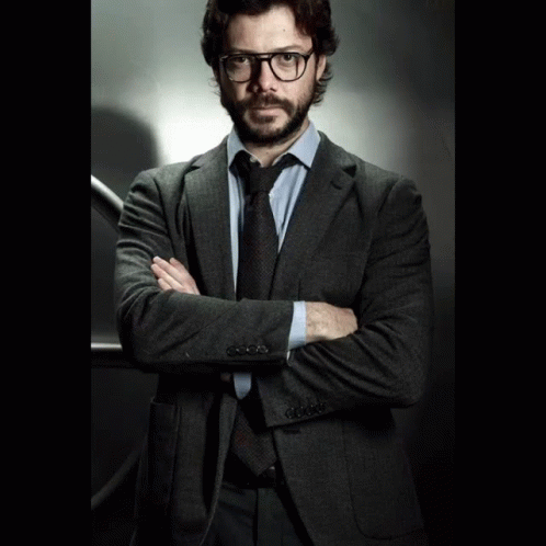 A Man In A Suit And Tie Stands With His Arms Crossed In Front Of A Vault Door GIF