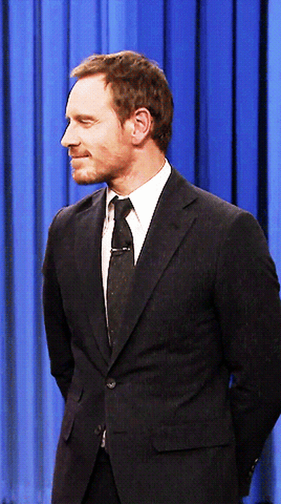 A Man In A Suit And Tie Stands With His Hands Behind His Back GIF