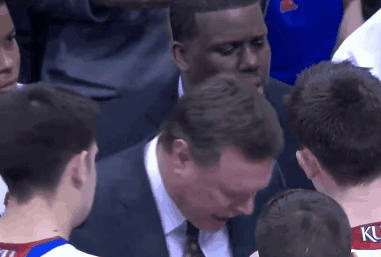 A Man In A Suit And Tie Talks To A Group Of Basketball Players Including One Wearing A Ku Jersey GIF