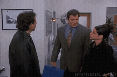 A Man In A Suit And Tie Talks To A Woman In A Black Jacket GIF