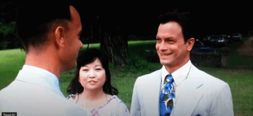 A Man In A Suit And Tie Talks To Another Man And A Woman GIF
