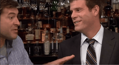 A Man In A Suit And Tie Talks To Another Man In A Bar GIF