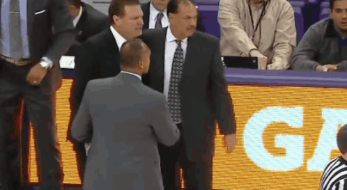 A Man In A Suit And Tie Talks To Another Man In Front Of A Sign That Says " Ga " GIF