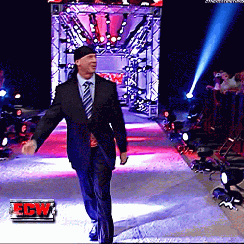 A Man In A Suit And Tie Walks Down A Red Carpet With A Ew Logo In The Corner GIF