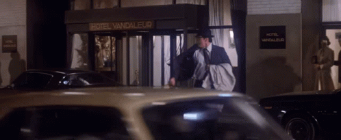 A Man In A Suit And Tie Walks In Front Of A Hotel Vandaleur GIF