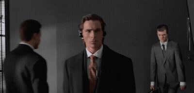 A Man In A Suit And Tie Wearing Headphones Stands In A Dark Room GIF