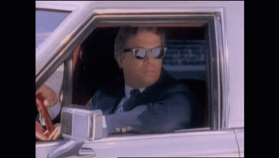 A Man In A Suit And Tie Wearing Sunglasses Is Driving A Car GIF