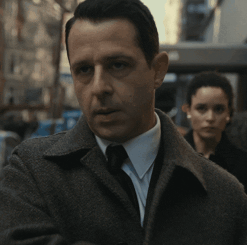 A Man In A Suit And Tie With A Woman In The Background GIF