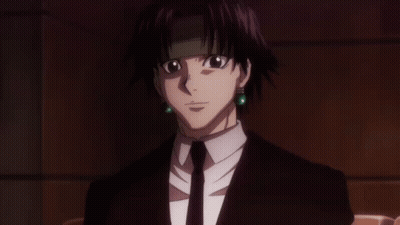 A Man In A Suit And Tie With Green Earrings Looks At The Camera GIF