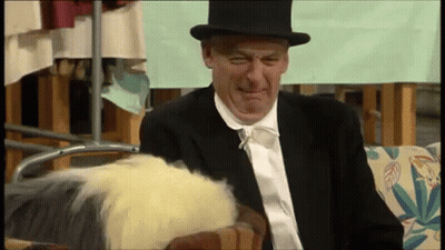 A Man In A Suit And Top Hat Is Sitting On A Couch . GIF