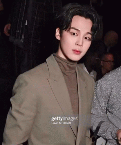 A Man In A Suit And Turtleneck Is Standing In Front Of A Crowd GIF