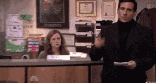 A Man In A Suit And Turtleneck Is Standing In Front Of A Woman At A Counter In An Office . GIF