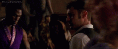 A Man In A Suit And Vest Is Looking At The Camera While Standing In A Crowded Room . GIF
