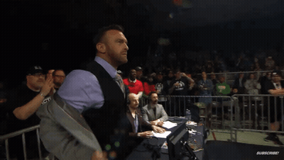 A Man In A Suit And Vest Stands In Front Of A Crowd With A Sign That Says ' Warriors ' On It GIF