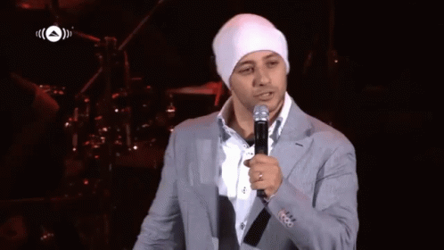 A Man In A Suit And White Hat Holds A Microphone In Front Of A Sign That Says ' A ' On It GIF
