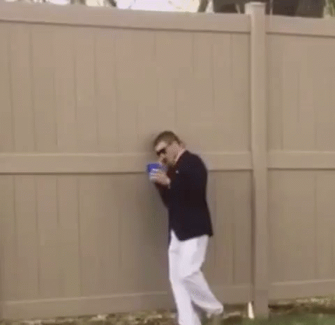A Man In A Suit And White Pants Is Standing Next To A Fence In The Grass . GIF