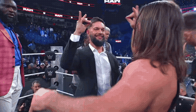A Man In A Suit And White Shirt Is Giving A High Five To Another Man In A Wrestling Ring . GIF