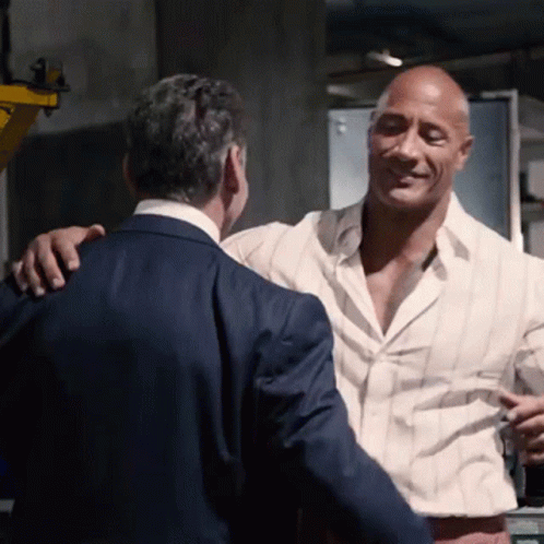 A Man In A Suit And White Shirt Is Hugging Another Man GIF