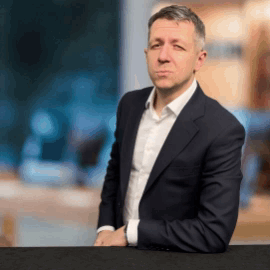 A Man In A Suit And White Shirt Is Leaning Against A Table GIF