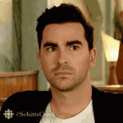 A Man In A Suit And White Shirt Is Making A Funny Face While Sitting In A Chair . GIF