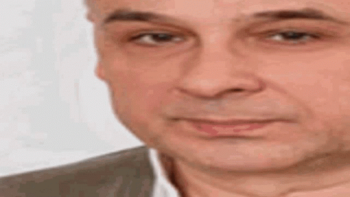 A Man In A Suit And White Shirt Is Making A Funny Face With His Hand On His Chin . GIF
