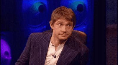 A Man In A Suit And White Shirt Is Sitting In A Chair In Front Of A Microphone . GIF