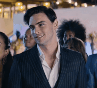 A Man In A Suit And White Shirt Is Smiling In A Crowd GIF