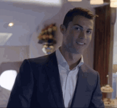 A Man In A Suit And White Shirt Is Smiling In A Room . GIF