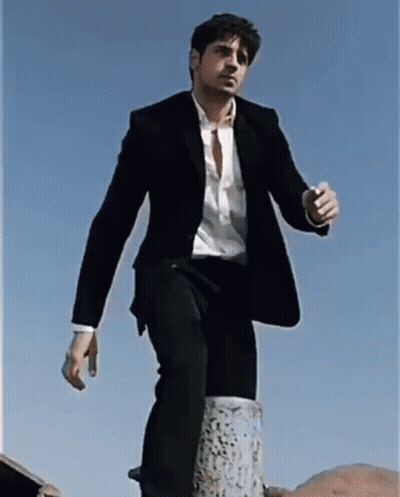 A Man In A Suit And White Shirt Is Standing On A Post GIF