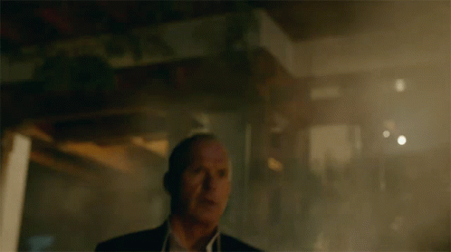 A Man In A Suit And White Shirt Stands In A Dark Room GIF