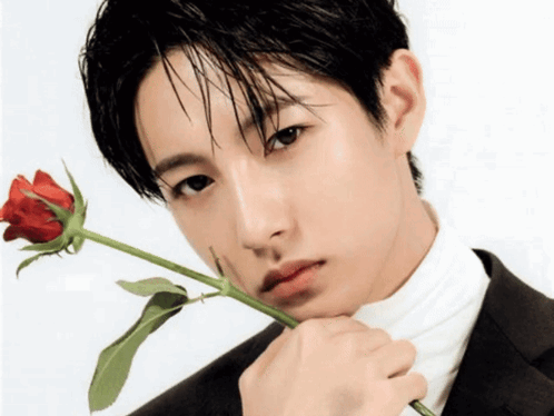 A Man In A Suit And White Turtleneck Holds A Red Rose To His Face GIF