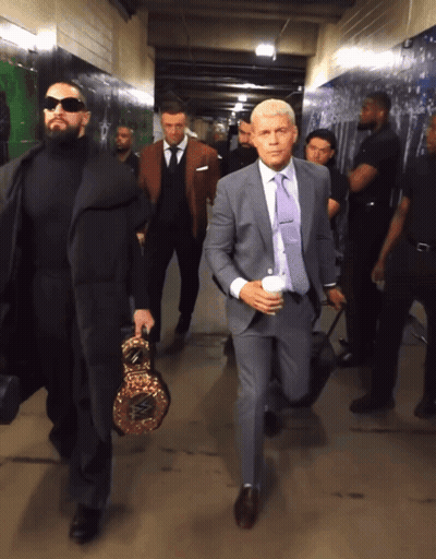 A Man In A Suit Carrying A Boxing Ring Is Walking Down A Hallway GIF