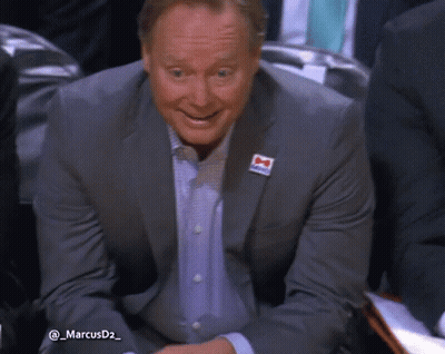 A Man In A Suit Has A Red White And Blue Ribbon On His Jacket With The Letter M On It GIF