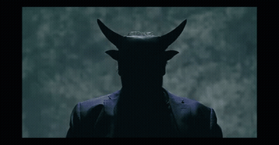 A Man In A Suit Has Horns On His Head In A Dark Room GIF