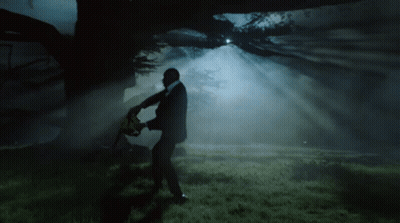A Man In A Suit Holding A Chainsaw In A Dark Forest GIF