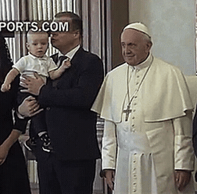 A Man In A Suit Holds A Baby In Front Of A Man In A White Robe With The Words Ports.com On The Bottom Right GIF