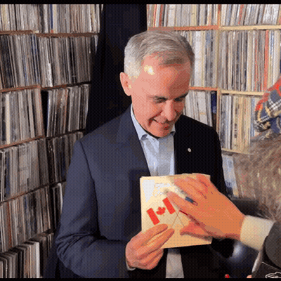 A Man In A Suit Holds A Canadian Flag In His Hand GIF
