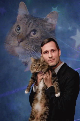 A Man In A Suit Holds A Cat In Front Of A Cat 'S Face GIF
