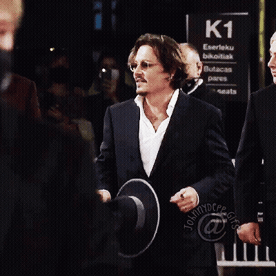 A Man In A Suit Holds A Hat Over His Face In Front Of A Sign That Says K1 GIF