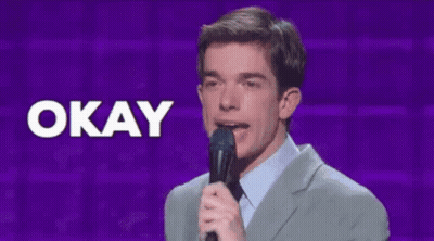 A Man In A Suit Holds A Microphone In Front Of A Sign That Says Okay GIF