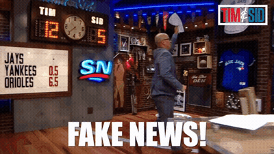 A Man In A Suit Holds A Piece Of Paper In Front Of A Scoreboard That Says Fake News GIF