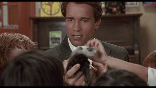 A Man In A Suit Holds A Small Animal In Front Of A Group Of Children GIF