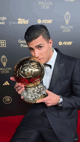 A Man In A Suit Holds A Soccer Ball In Front Of A Wall That Says Ballon Dor GIF