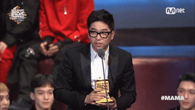 A Man In A Suit Holds A Trophy In Front Of A Microphone At A Music Awards GIF