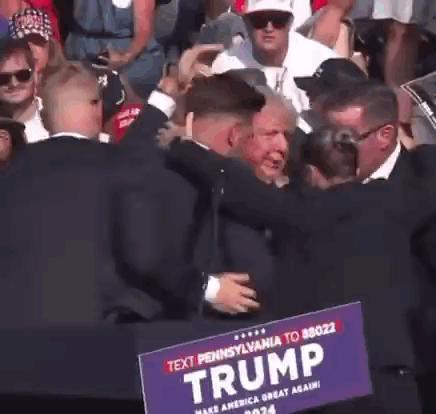 A Man In A Suit Holds A Trump Sign In Front Of A Crowd GIF